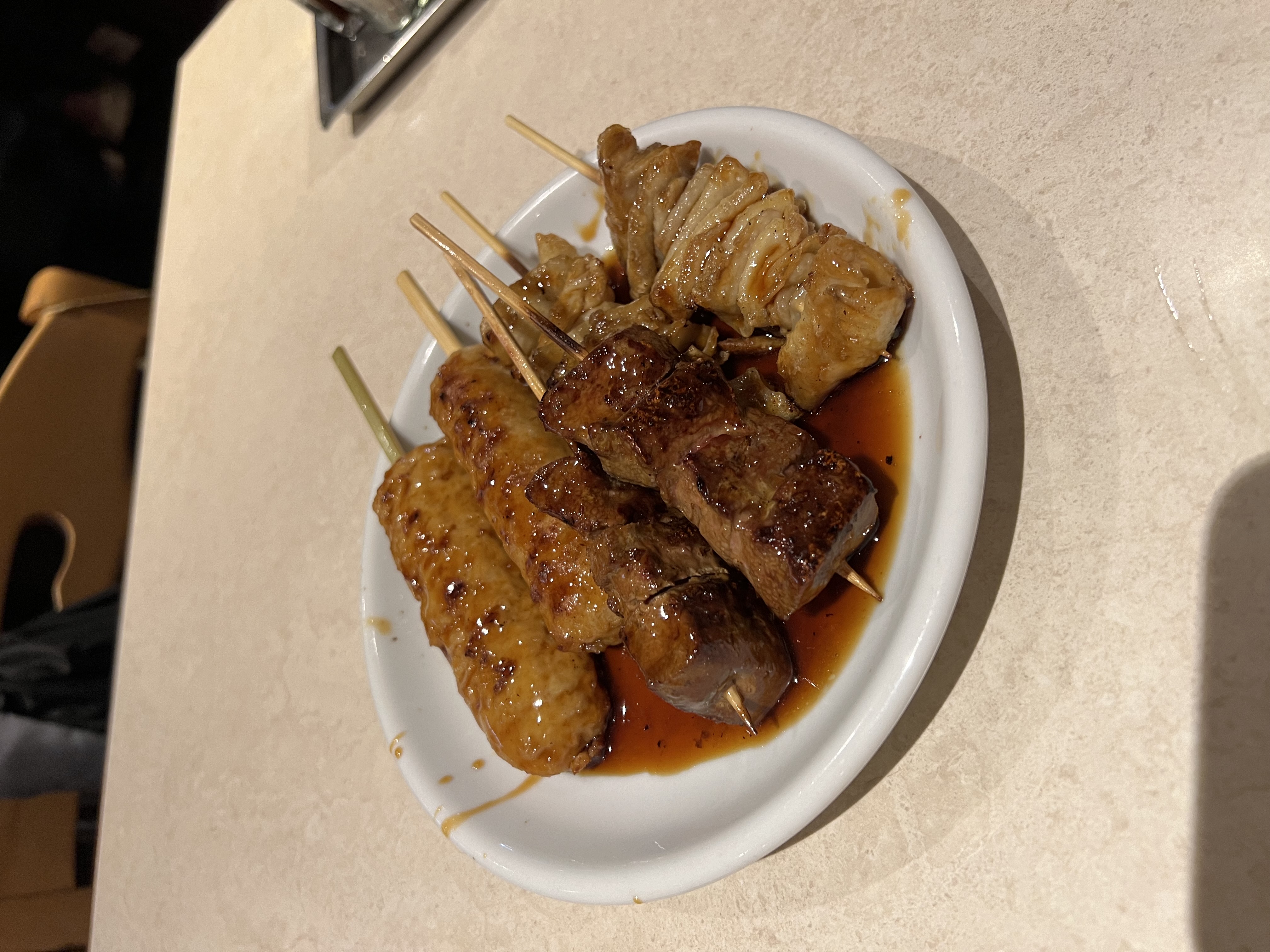 Yakitori skewers glazed with tare sauce on a white plate at Ohyama