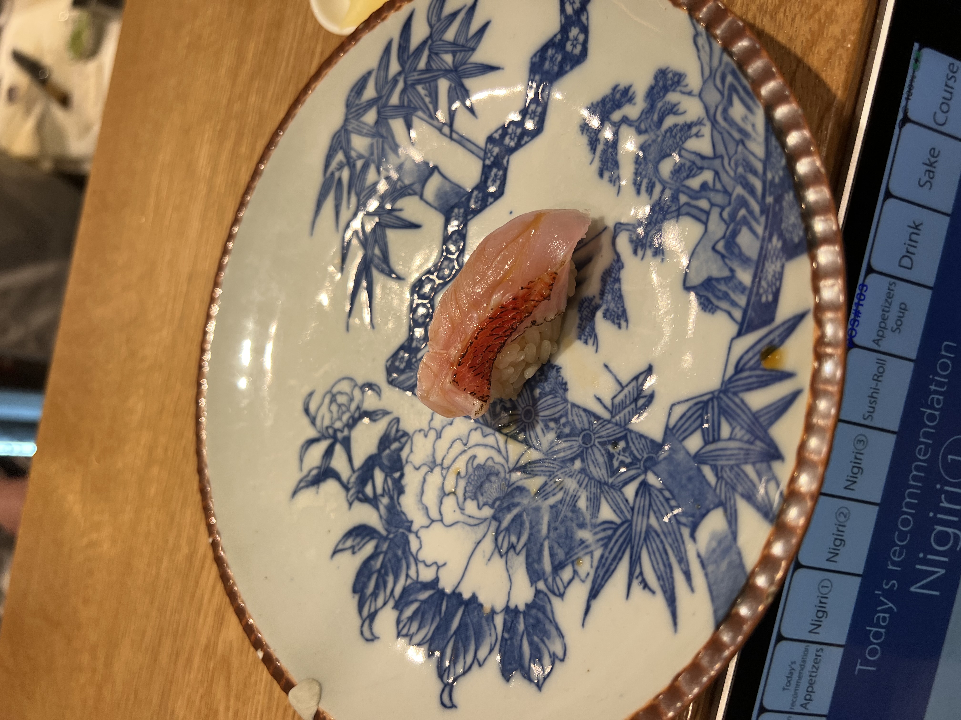 Fish nigiri on a blue and white ceramic plate with today's recommendation visible on the iPad