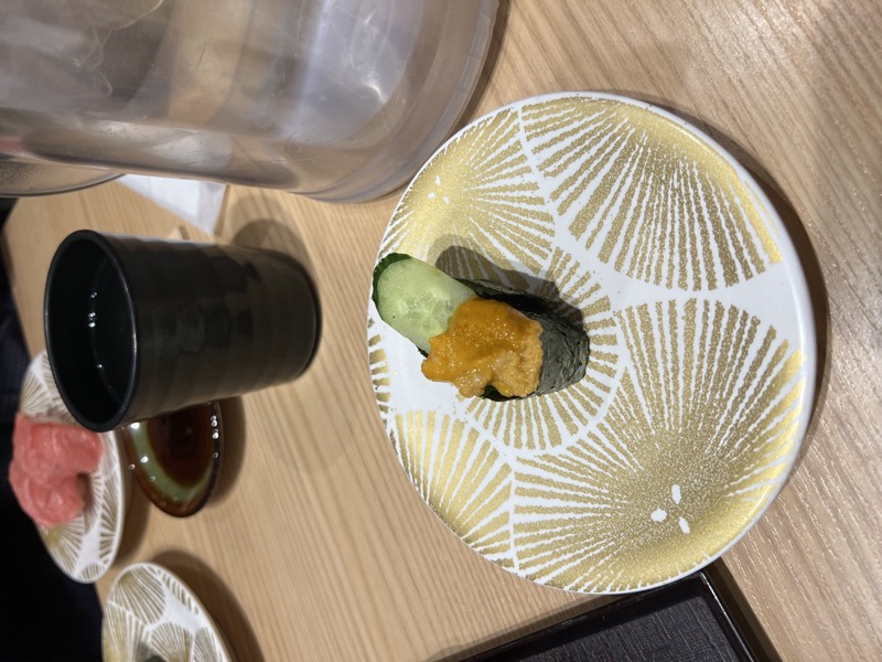 Uni on cucumber topped with salmon roe on a gold-patterned ceramic plate, with miso soup alongside