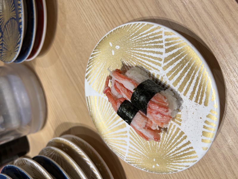 Snow crab nigiri on a gold-patterned plate, stack of finished plates in background