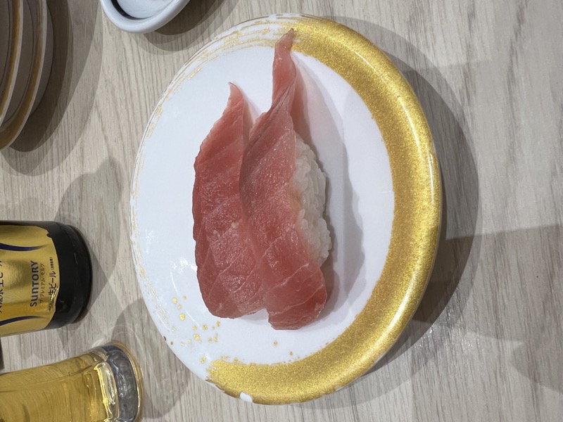 Two pieces of tuna nigiri on a gold-rimmed white plate with a Suntory beer