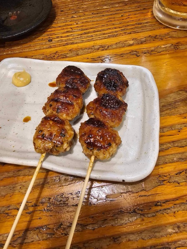 Two tsukune chicken meatball skewers on a white ceramic plate with dipping sauce