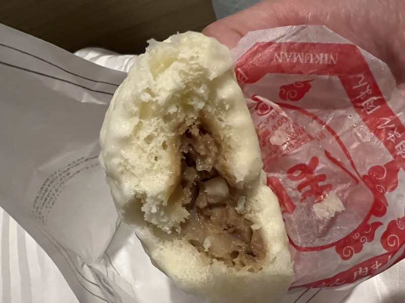 A nikuman steamed pork bun broken open to show the filling, wrapped in branded tissue paper